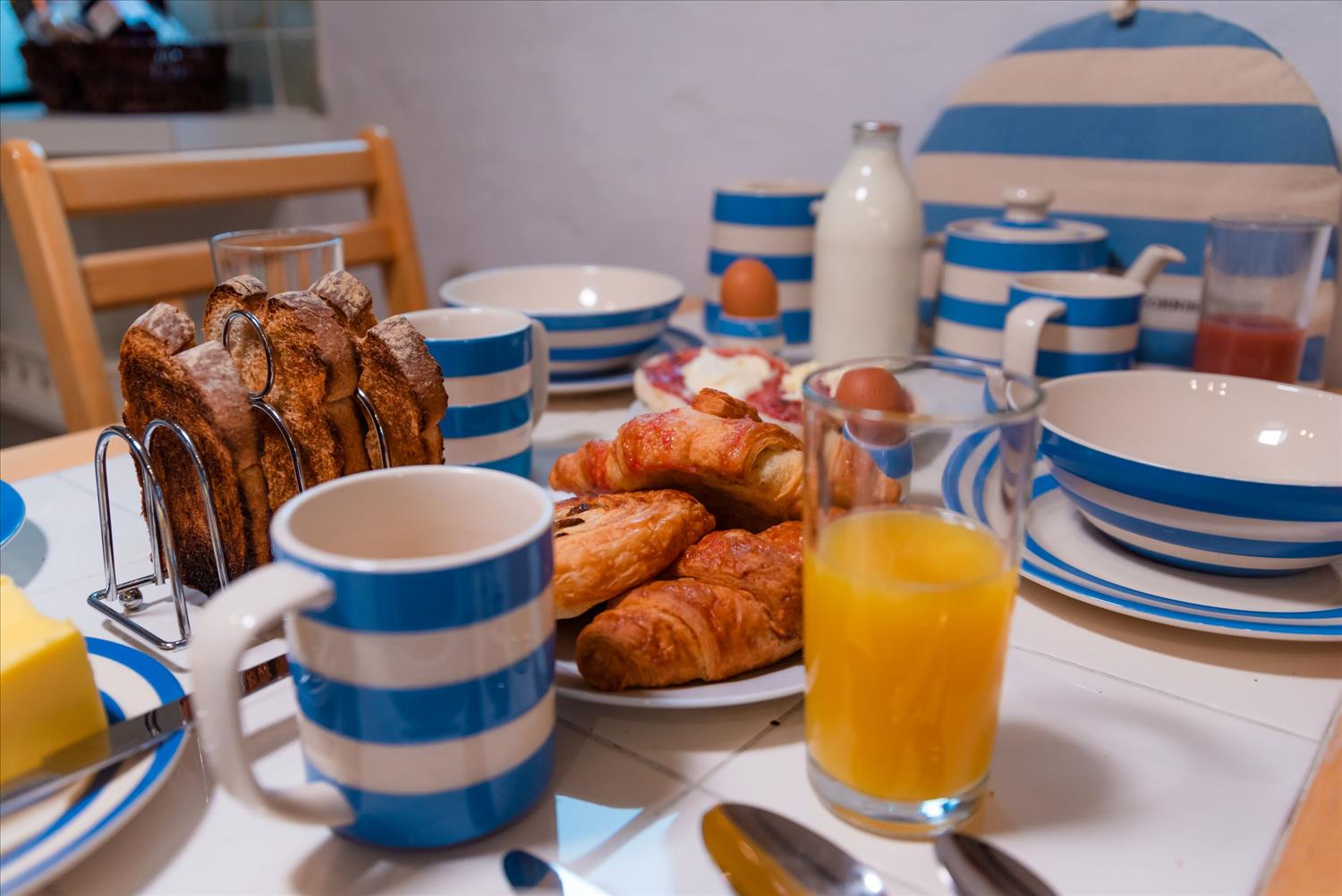 Close-up of a breakfast table at Polrunny Farm's Blackberry Cottage, with vintage blue and white Cornishware crockery, pastries, toast and juices.
