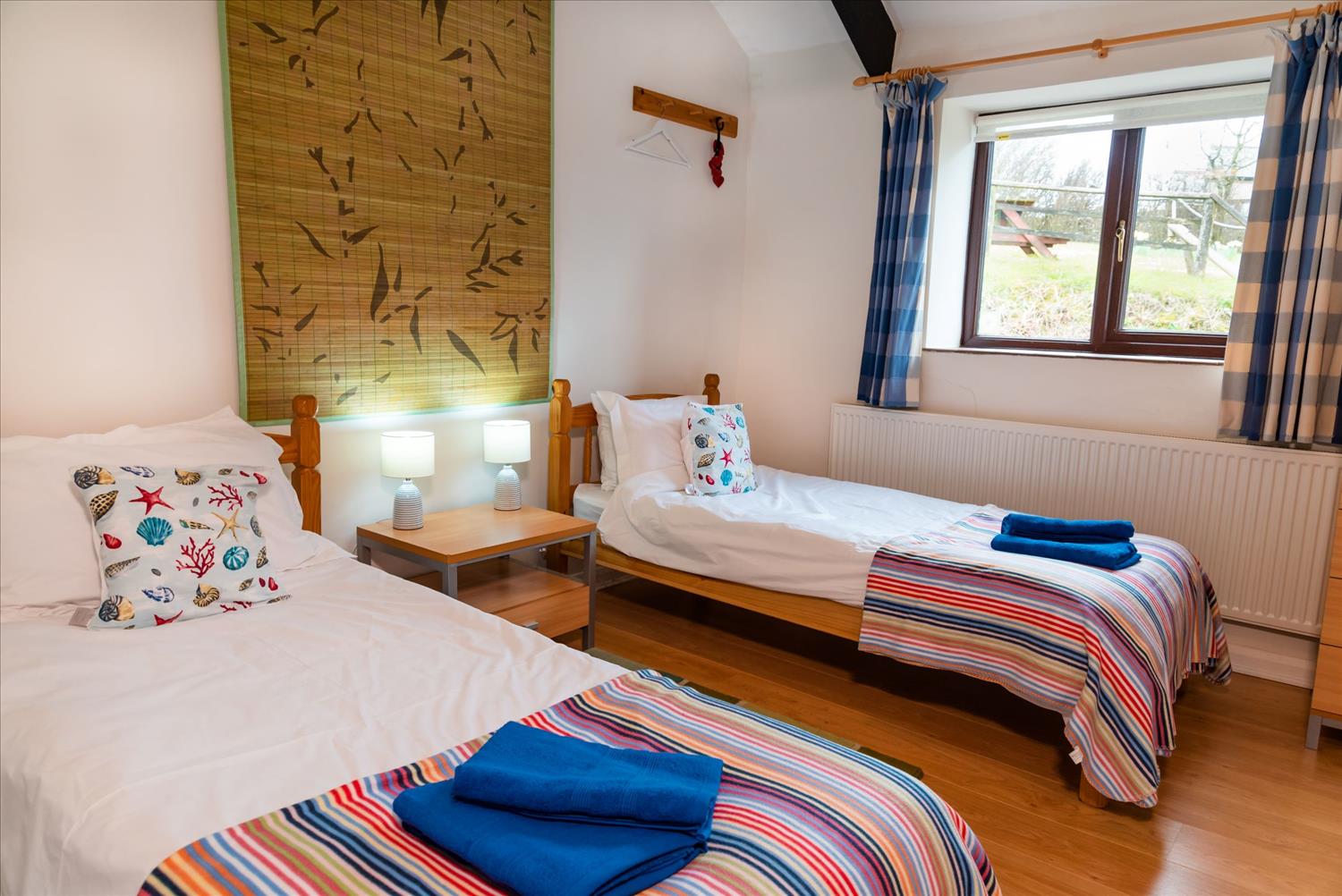 The twin bedroom at Polrunny Farm's Elderberry Cottage, with blue towels on the end of the beds, and a tapestry hung on the wall