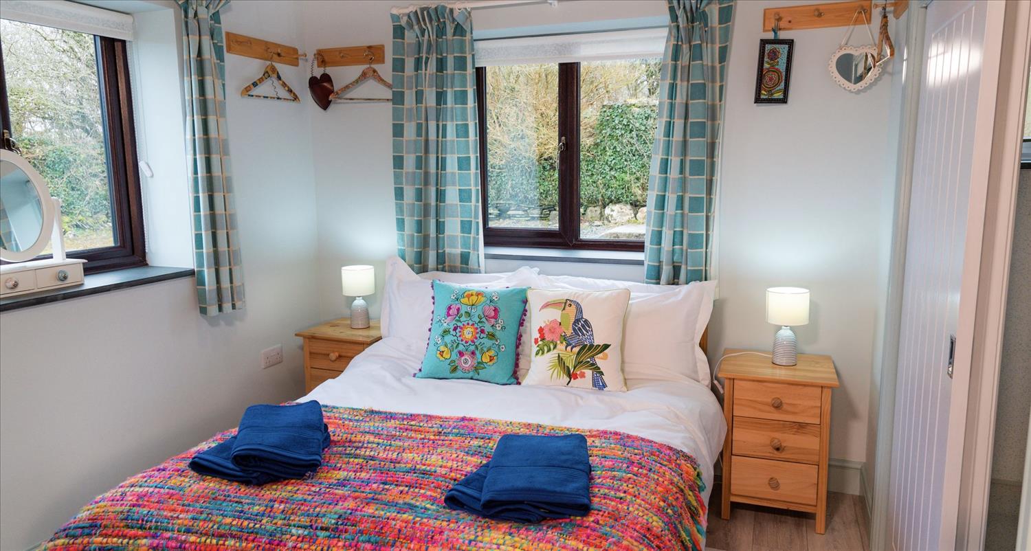 The double bedroom at Sloe Cottage, with blue towels on a purple, orange and blue bedspread, with two brightly coloured cushions at the head of the bed